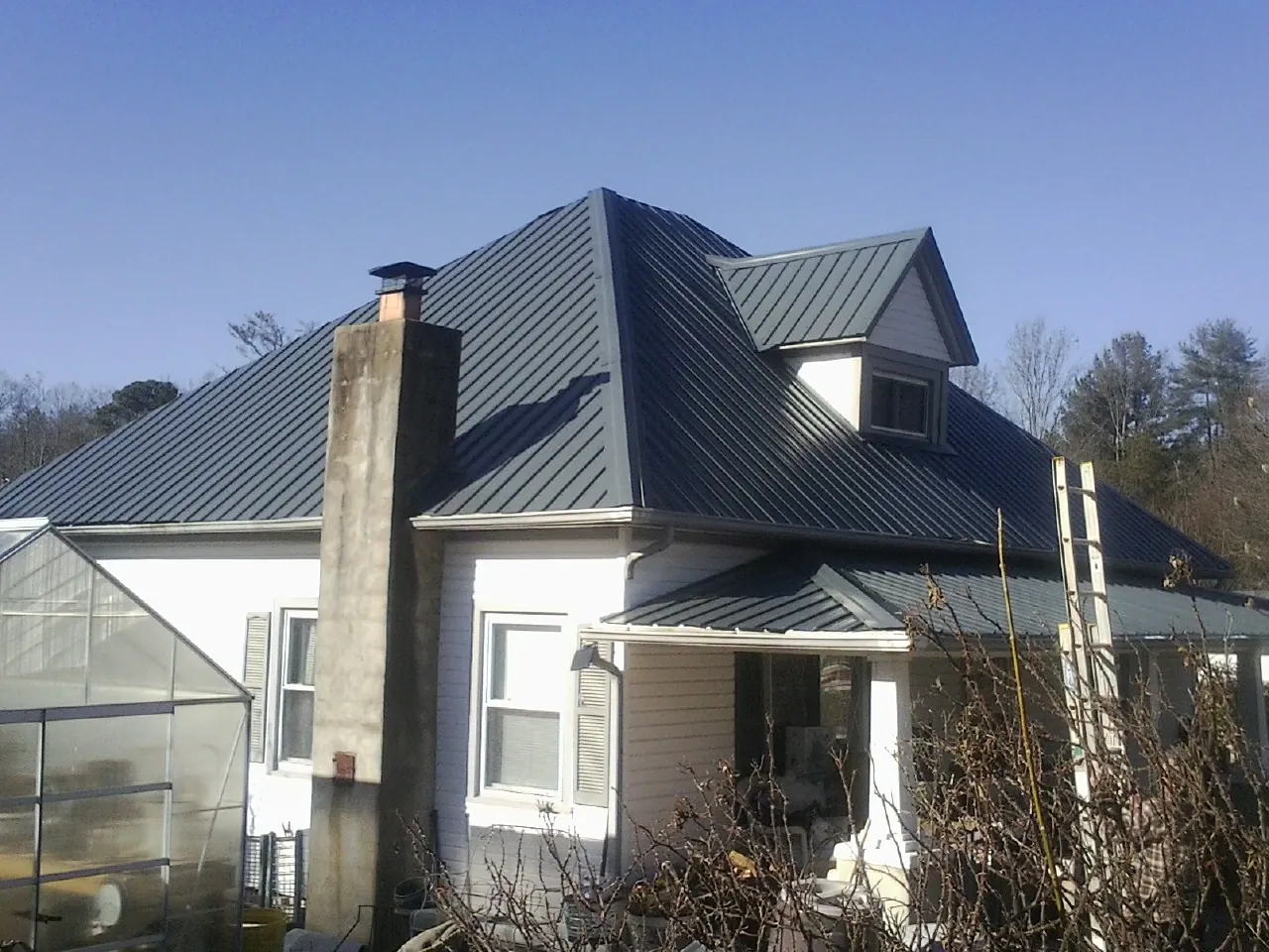 Dark blue standing seam metal roof on a white farmhouse with dormer — Slate & Tile Roof Repair by Roofing Brothers in Seward