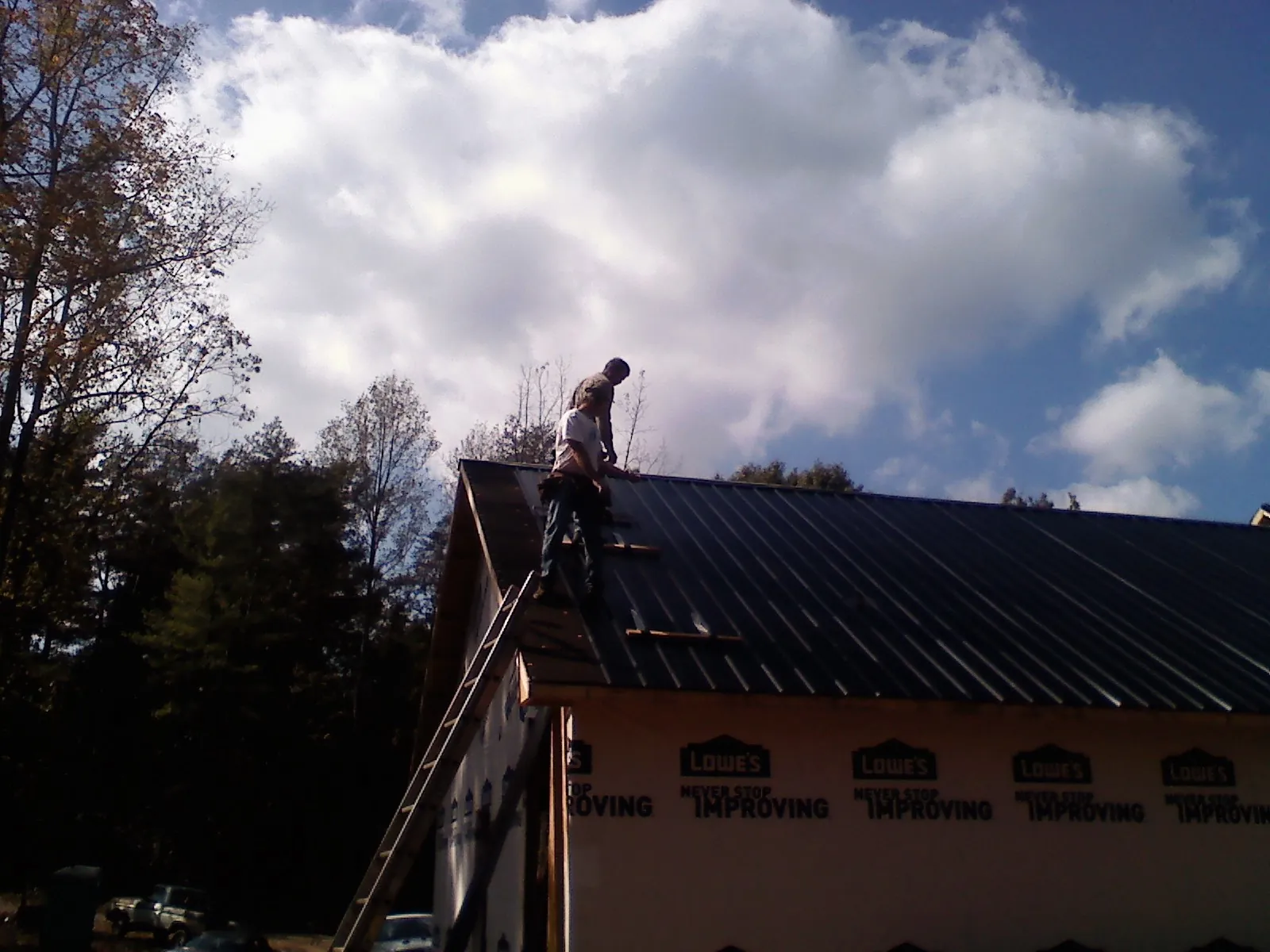 Roofer fastening dark metal panels high against a cloudy sky, from a Roof Inspection job in Seward
