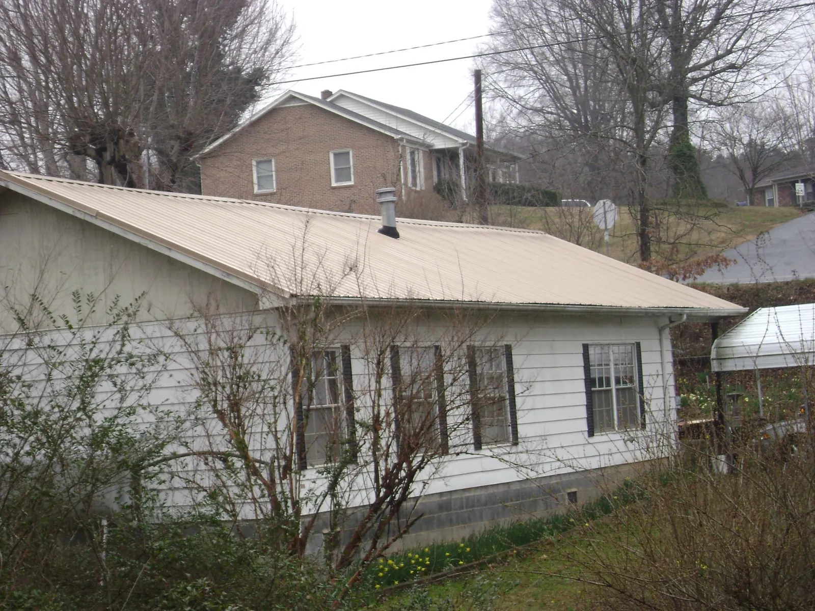 Tan metal roof on a white sided house set into a hillside — Commercial Roofing by Roofing Brothers in Seward